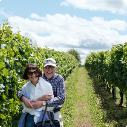elderly couple, man giving woman a back hug, standing outside vineyard