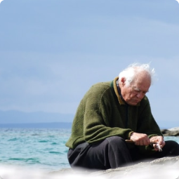 elderly man holding sticks while sitting at the beach